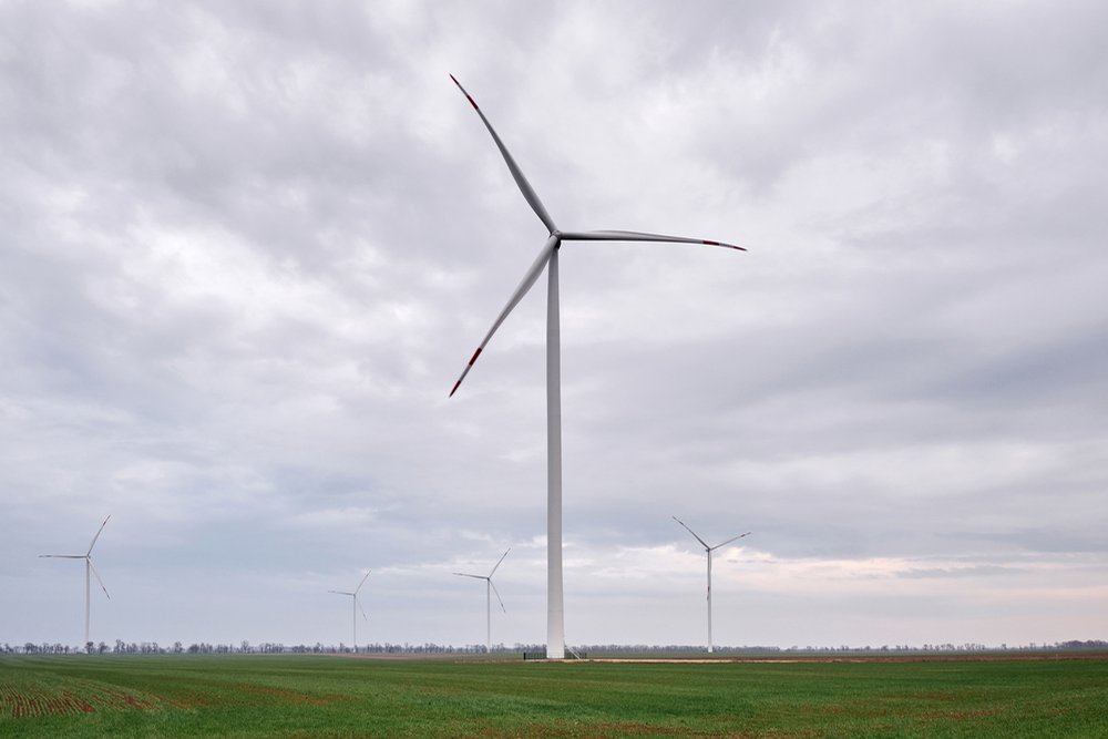 曇り空の下、緑の草原に立つ風力発電の風車