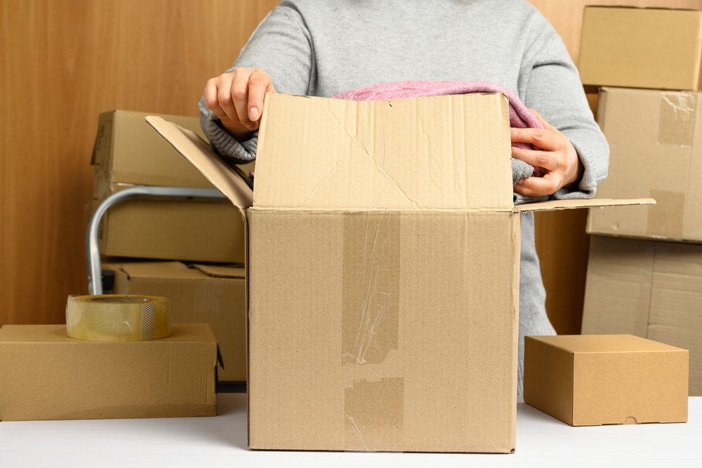 段ボール箱に入った服を取り出す手元と積まれた箱