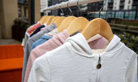 木のハンガーでラックに並ぶ淡い色の服