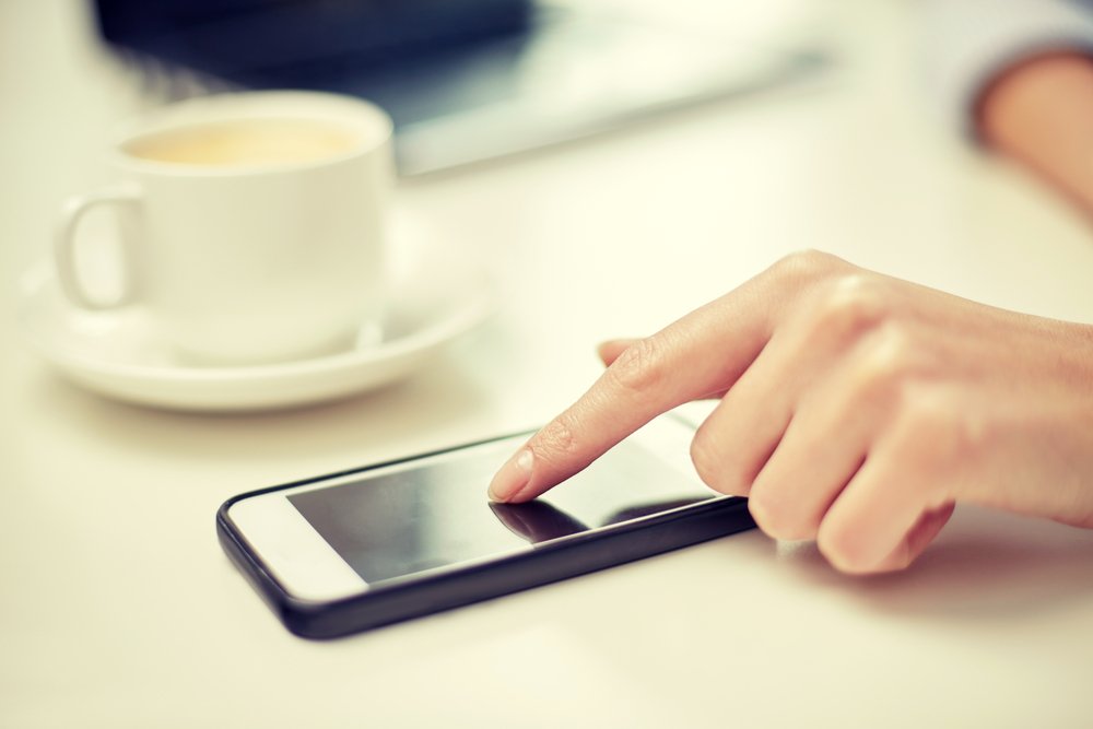 コーヒーカップの横でスマートフォンの画面に触れる手元