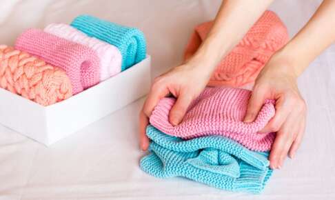 ニットを畳む手元と、畳んだ服が並ぶ白い収納箱
