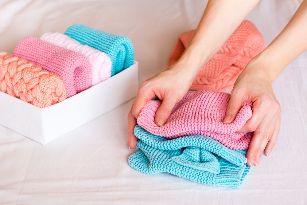 ニットを畳む手元と、畳んだ服が並ぶ白い収納箱