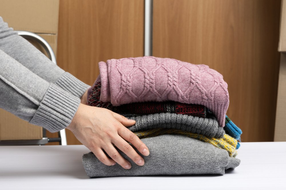 たたんで重ねたニットのセーターに手を添える様子