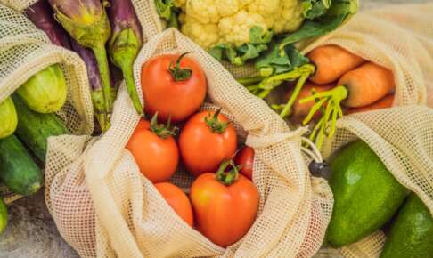 木の台に並ぶ、網の再利用袋に入ったトマトやにんじんなどの野菜