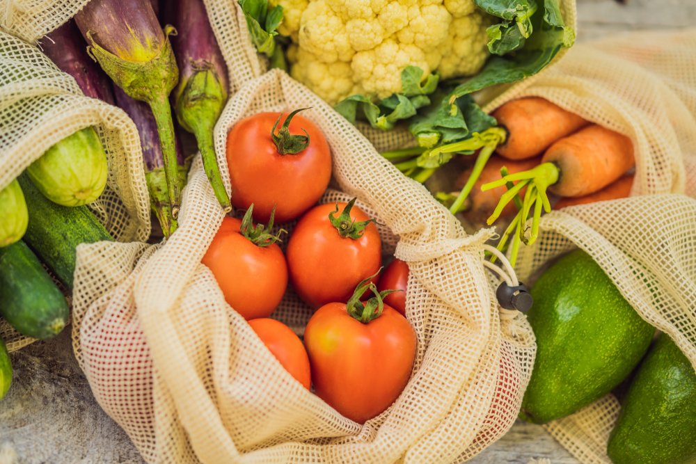 木の台に並ぶ、網の再利用袋に入ったトマトやにんじんなどの野菜
