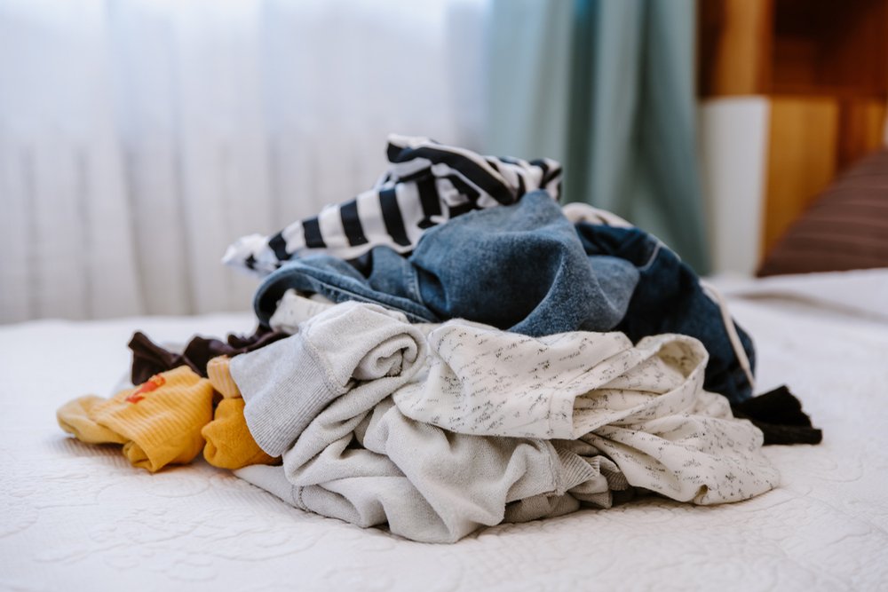 ベッドの上に積まれた、ニットやボーダーなどの脱いだ服の山