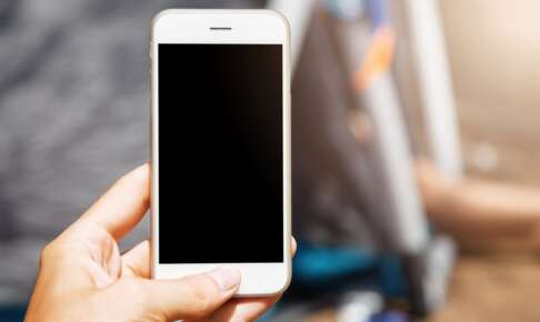 白いスマートフォンを片手に持ち、画面を見る手元