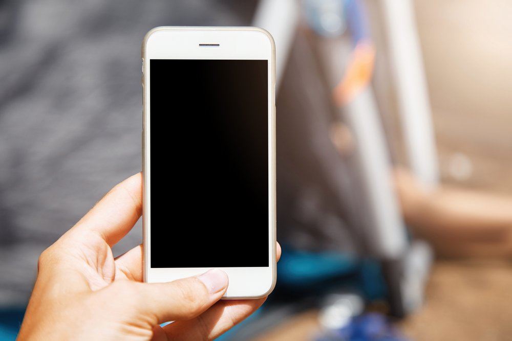 白いスマートフォンを片手に持ち、画面を見る手元