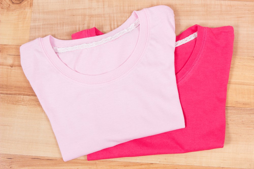 木の板の上にたたんで重ねた、薄いピンクと濃いピンクのTシャツ