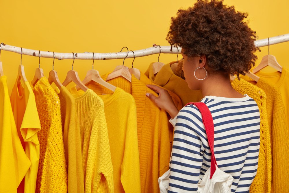 ハンガーに並ぶ黄色のニットや服を選ぶ女性の後ろ姿