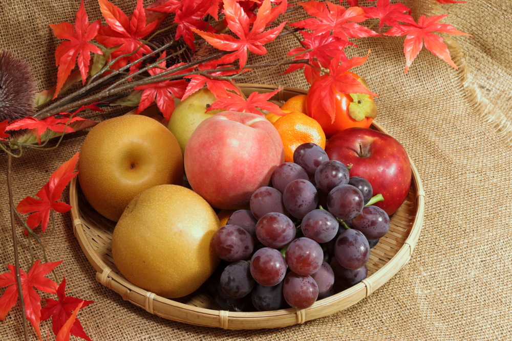竹ざるに盛られた梨やぶどうなど秋の果物の詰め合わせと紅葉