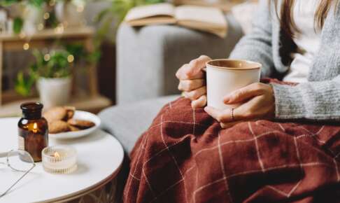 ひざ掛けにくるまり、温かい飲み物を手に体を温める様子