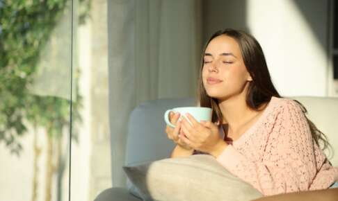 窓辺で温かい飲み物を手に、穏やかに過ごす女性